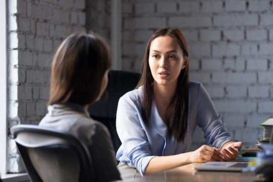 two women consult at table in front of a brick wall